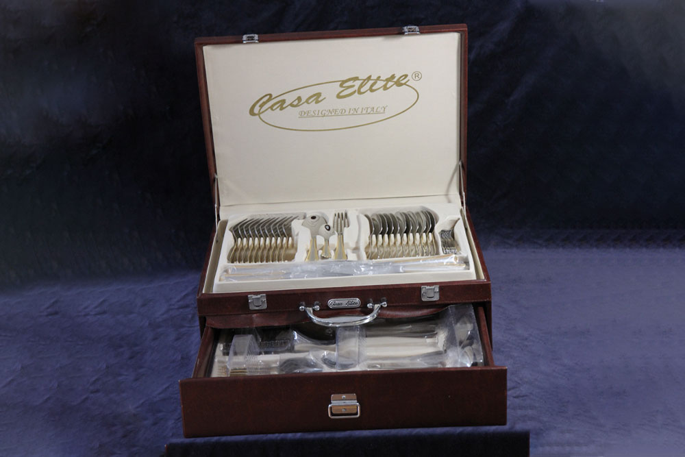 A luxurious cutlery set displayed in an open brown leather case. The case's lid reads "Casa Ette" and "Designed Perfect." The set includes neatly arranged forks, knives, and spoons with a polished finish. With compartments and a handle for easy transport, it makes a perfect donation for charity events.