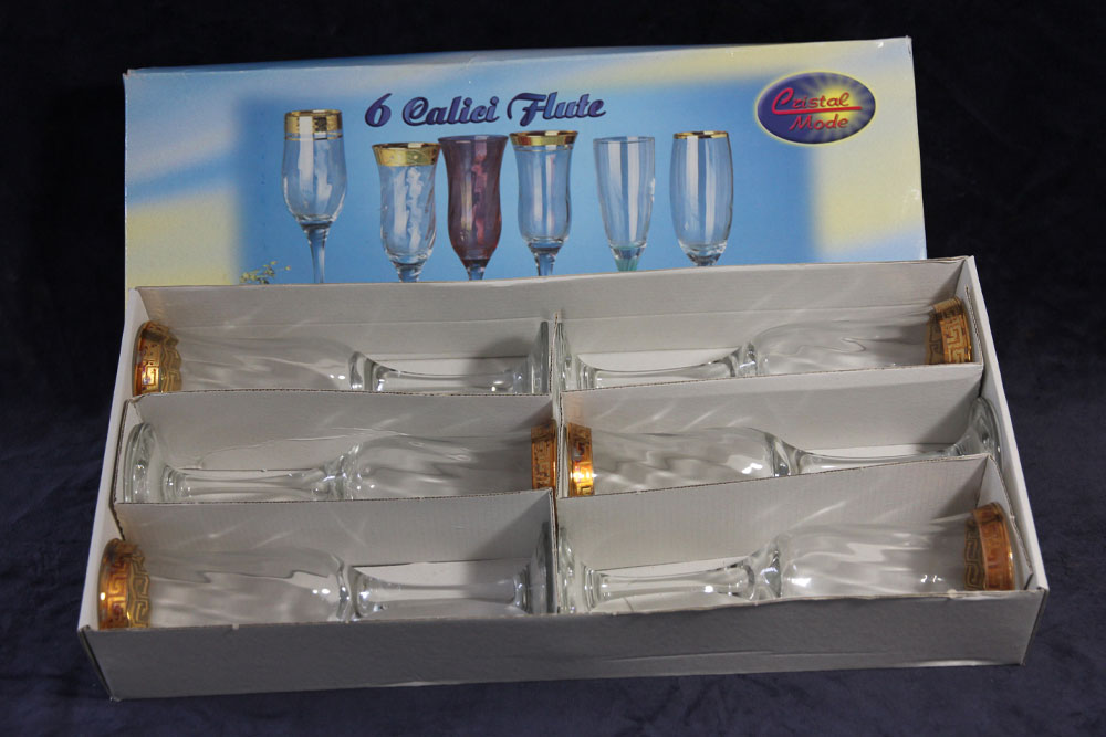 A set of six crystal flute glasses in a box. The box displays images of six glasses, some with colored liquid against a blue background. The glasses, perfect for toasting with water or champagne, have gold rims and are organized in two rows of three. The label reads "6 Calici Flute" and "Crystal Mode.