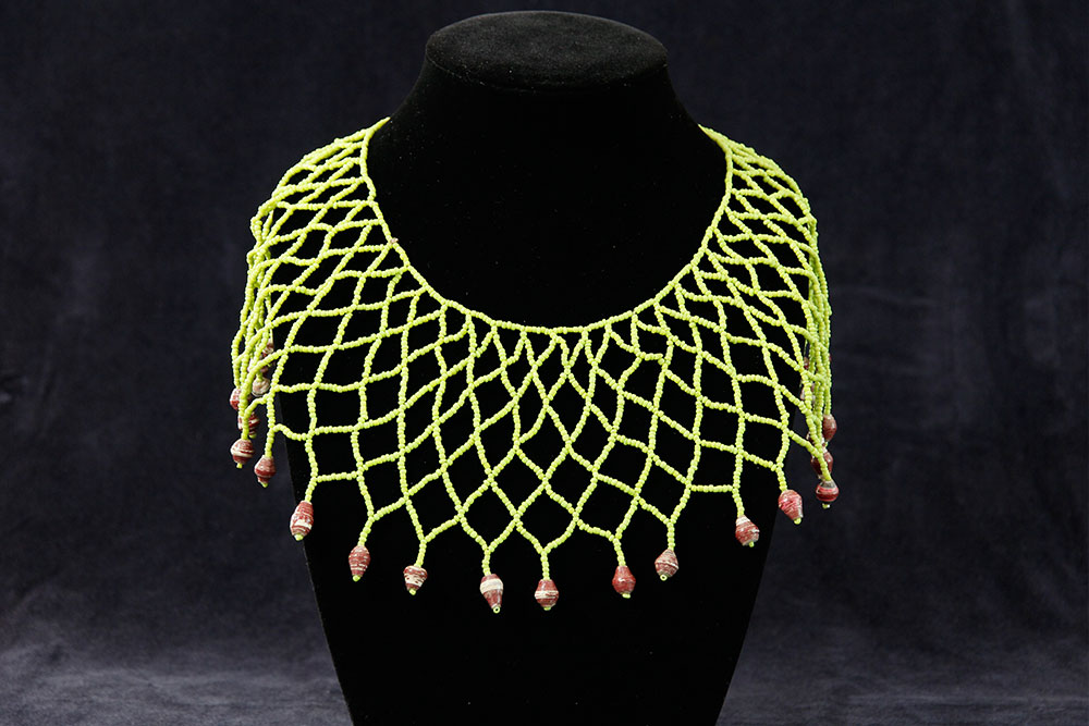 A black display bust showcasing a handmade necklace with an intricate netted design made of bright green cords. The lower edge of the net is adorned with spaced, dangling beads of a reddish-brown hue. The background is a plain dark color, highlighting this unique piece available for charity donation.